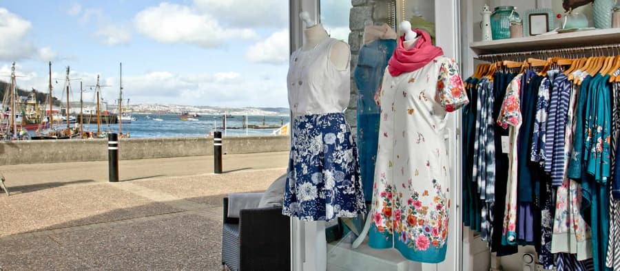 Dresses hanging in the doorway of Bertie and Crew with the Brixham Marina water visible beyond.